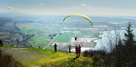 people paragliding off a cliff overlooking fields and a lake