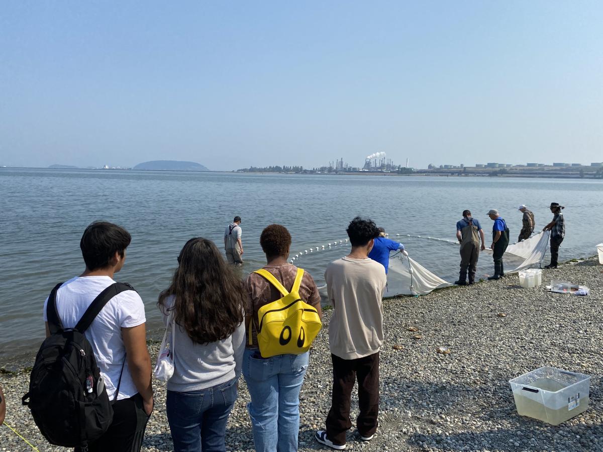 Young people stand on a beach while adults bring in a net from the water