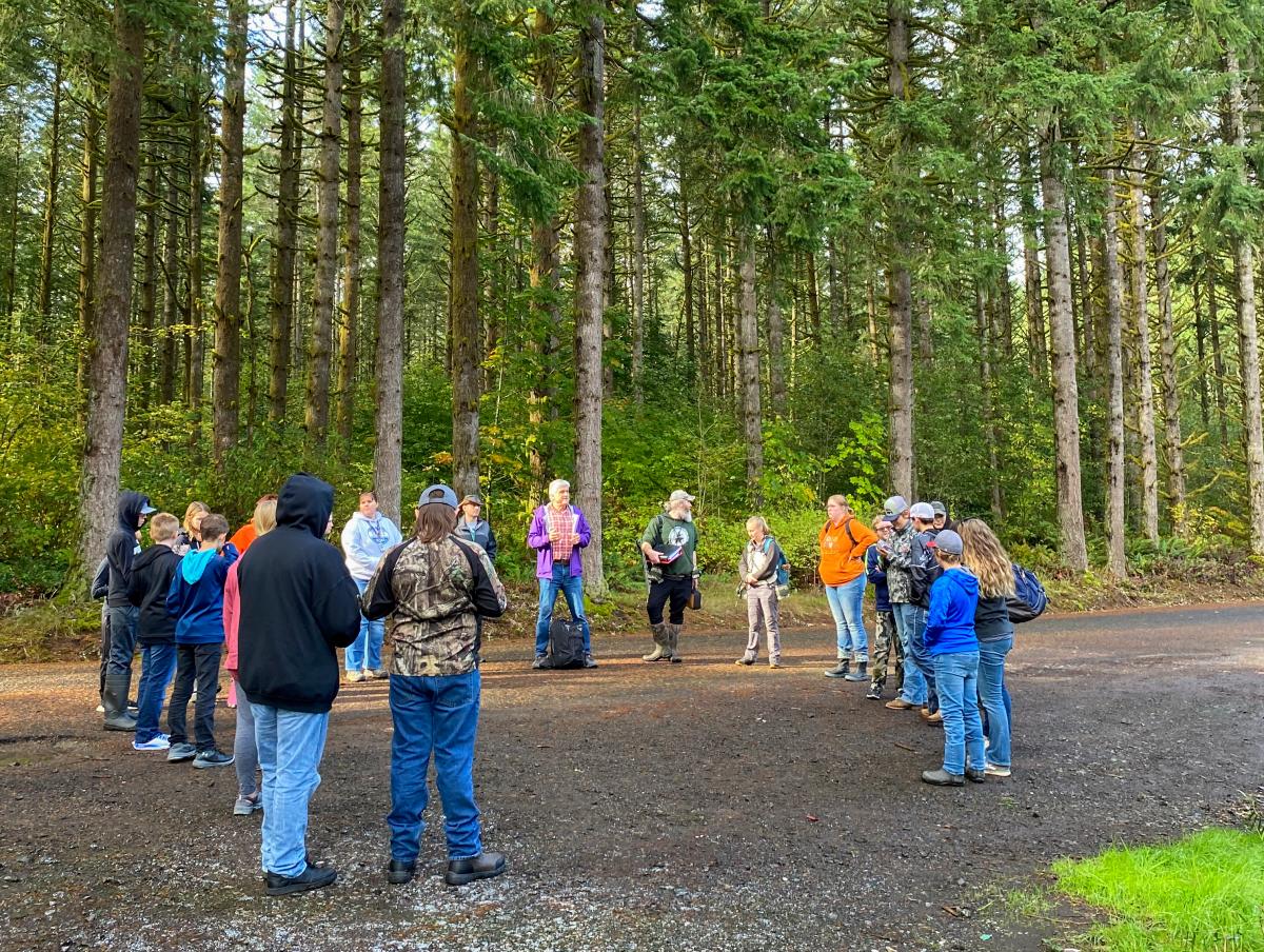 Youth and adults stand in a semi-circle in the woods at Toutle Lake